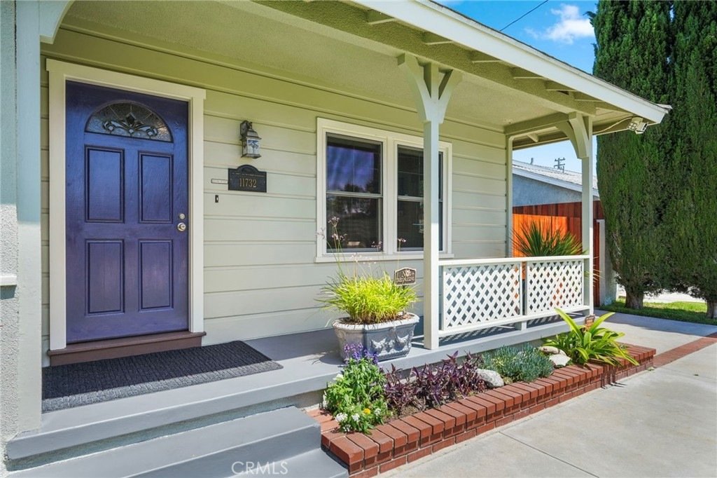 Front house on Kathy Ln, Garden Grove, CA, featuring a deep blue door, white window, and brick-bordered flowerbed.