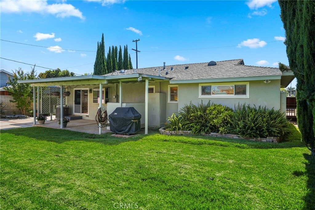 Suburban backyard on Kathy Ln, Garden Grove, CA, featuring a beige house, covered patio, BBQ grill, and green lawn.