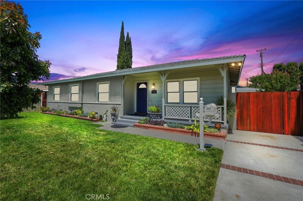 Gray house on Kathy Ln, Garden Grove, CA, featuring a front porch, lush garden beds, and a purple sunset sky.
