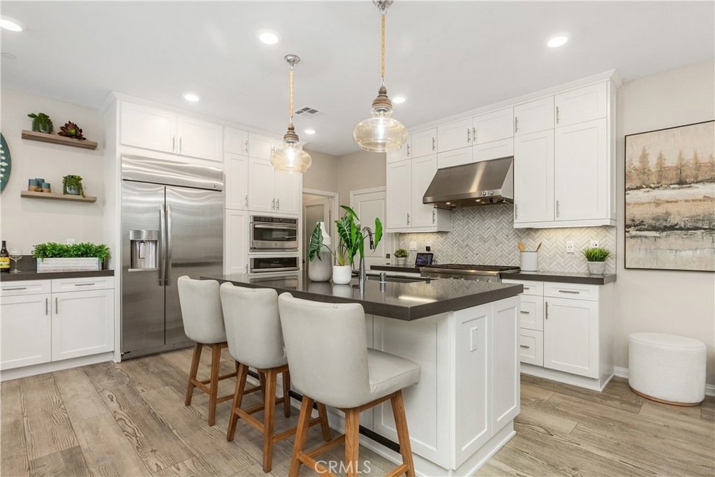 Modern kitchen on Veraz Rd, Rancho Mission Viejo, CA, featuring white cabinets, stainless steel appliances, a central island, and beige chairs.