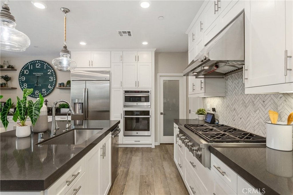 Modern kitchen on Veraz Rd, Rancho Mission Viejo, CA, featuring white cabinets, dark countertops, stainless steel appliances, and a large wall clock.