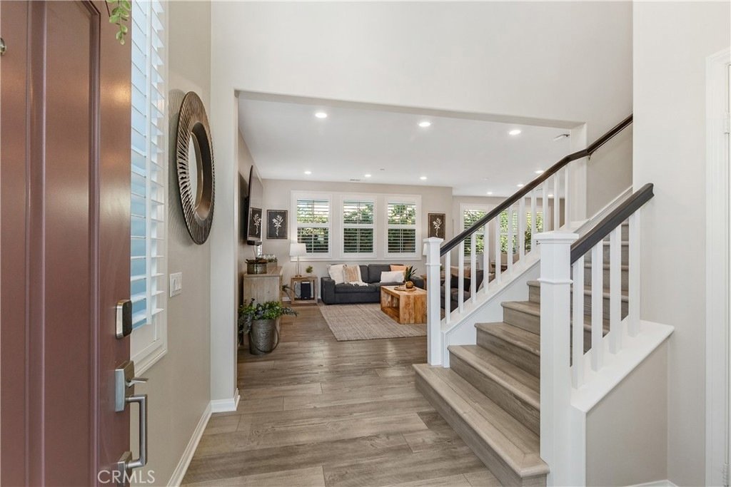 Spacious living room on Veraz Rd, Rancho Mission Viejo, CA, featuring wooden floors, gray sofas, a rustic coffee table, and a white-banister staircase.