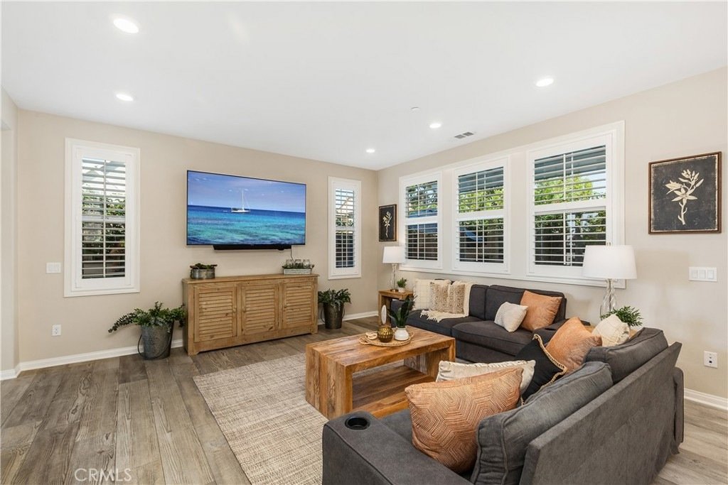 Living room on Veraz Rd, Rancho Mission Viejo, CA, featuring a gray sectional sofa, orange cushions, and a wall-mounted TV over a wooden cabinet.