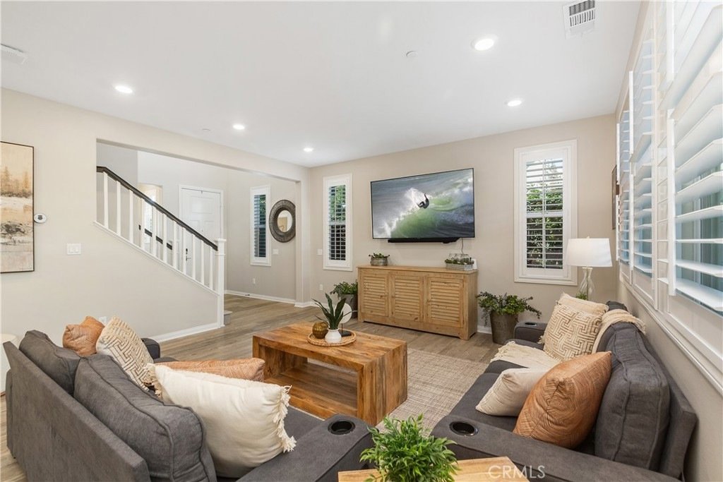 Living room on Veraz Rd, Rancho Mission Viejo, CA, featuring gray sofas, a wooden coffee table, and a wall-mounted TV displaying a surfing scene.