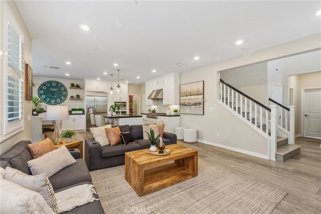 Living room on Veraz Rd, Rancho Mission Viejo, CA, featuring a gray sofa, wooden coffee table, large wall clock, and white kitchen.