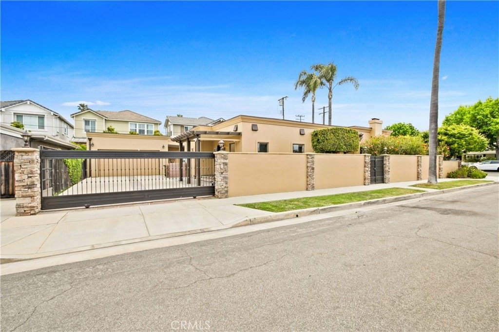 Modern California home on Tustin Ave in Costa Mesa with beige walls, stone accents, and a tall security gate.