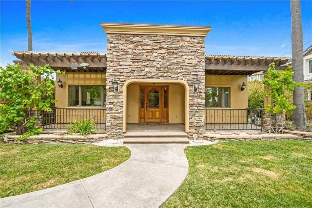 Single-story California home on Tustin Ave in Costa Mesa featuring a stone facade, wooden door, and twin palm trees.