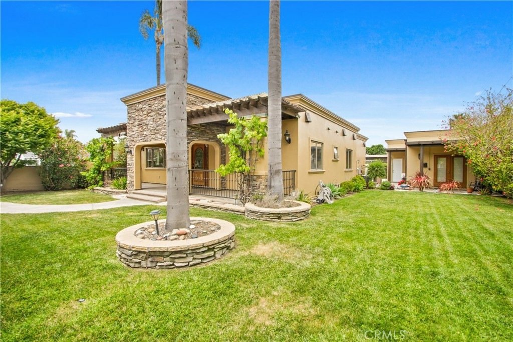 Single-story California home on Tustin Ave in Costa Mesa featuring a tan stucco and stone facade, lush lawn, and palm trees.
