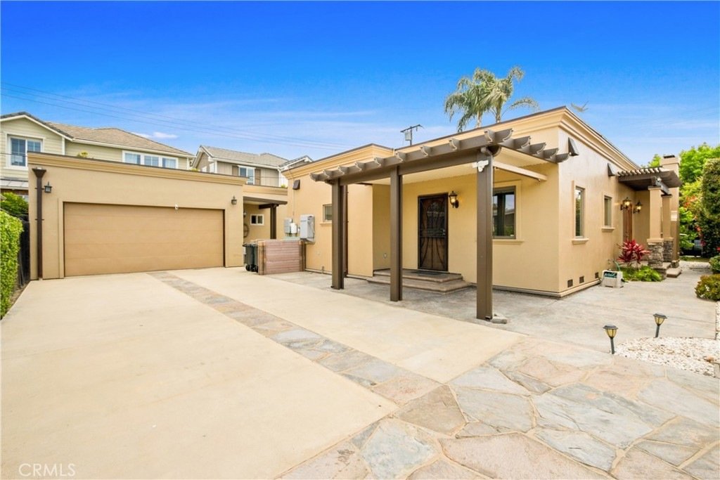 Modern single-story California home on Tustin Ave in Costa Mesa featuring beige stucco, a wooden pergola, and a two-car garage.