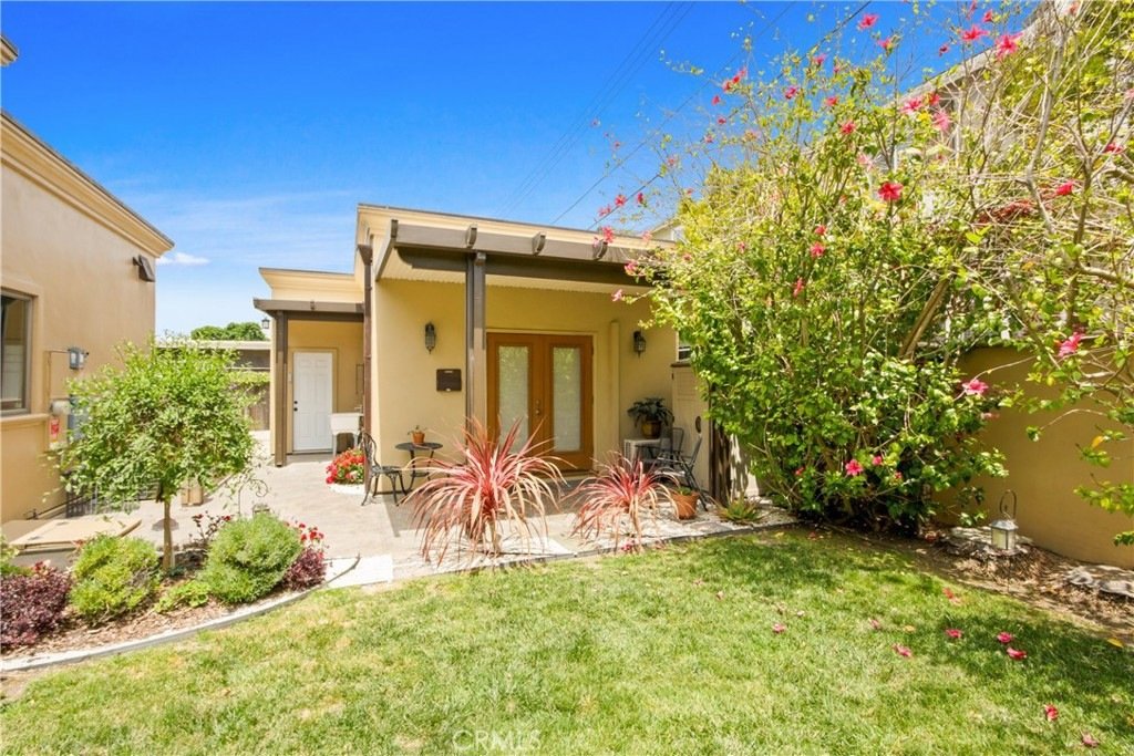 Cozy California backyard on Tustin Ave in Costa Mesa featuring a beige guest house with French doors and lush flowering landscaping.