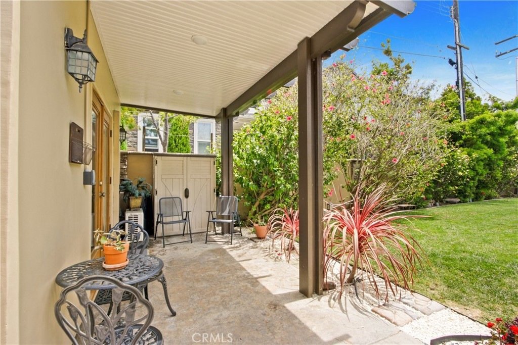 California covered patio on Tustin Ave in Costa Mesa featuring black metal furniture, potted plants, and a lush garden view.