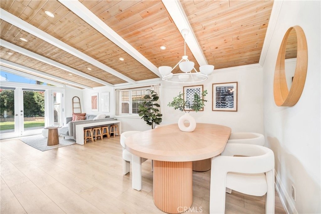 Dining area on Hanover Dr, Costa Mesa, CA, with a light wood table, white chairs, wood ceiling beams, and a large window.