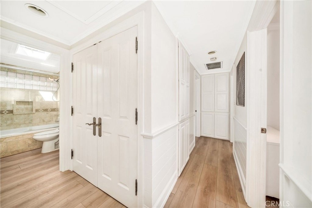 Bright hallway on Hanover Dr, Costa Mesa, CA, with light wood floors, white walls, and a double door leading to a bathroom.