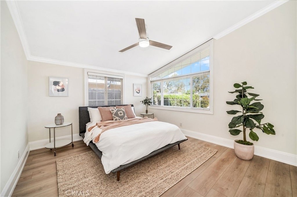 Bedroom on Hanover Dr, Costa Mesa, CA, with a large bed, white and beige blankets, a plant, and a ceiling fan.