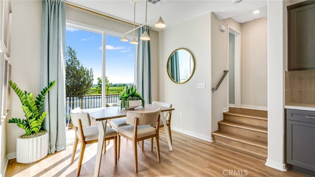 Dining area on Montoya Paseo, Ontario, CA, with a light wood table, four chairs, blue curtains, houseplants, and a round mirror.