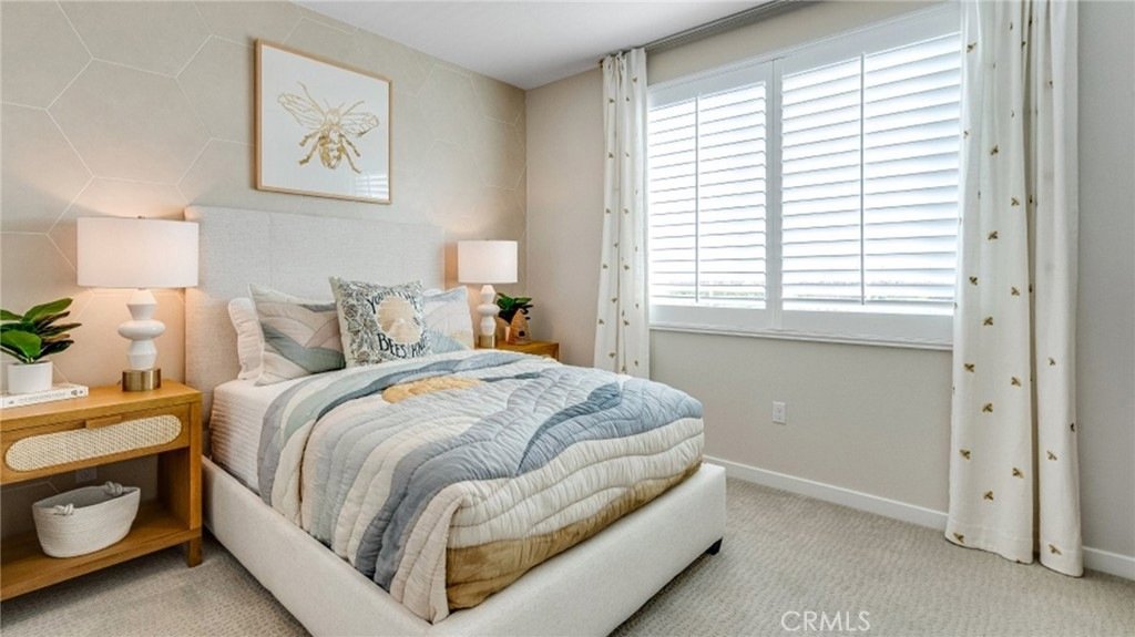 Bedroom on Montoya Paseo, Ontario, CA, with a patterned quilt, bee-themed decor, indoor plants, and large windows.