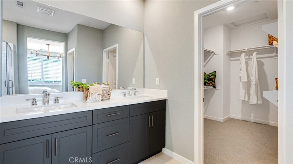 Bathroom on Montoya Paseo, Ontario, CA, with two sinks, a dark vanity, a large mirror, and a walk-in closet with white robes.
