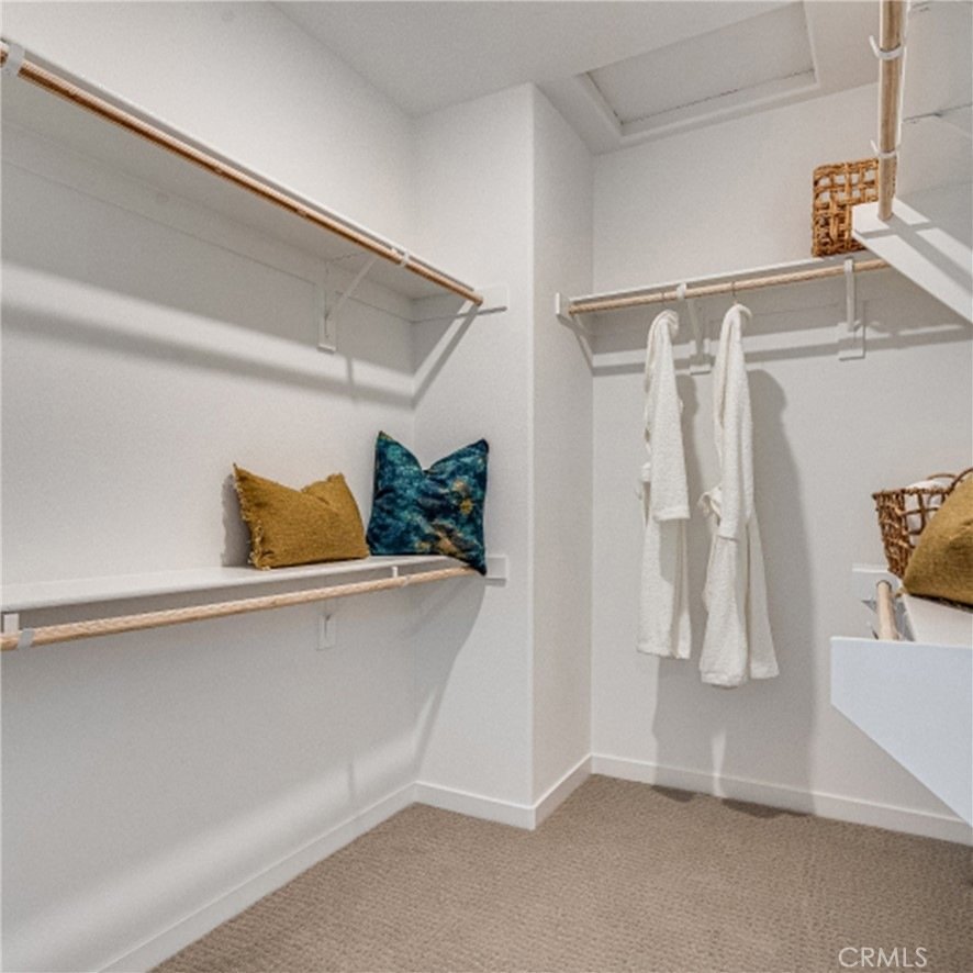 Walk-in closet on Montoya Paseo, Ontario, CA, with beige carpet, wooden shelves, hanging rods, and white robes.