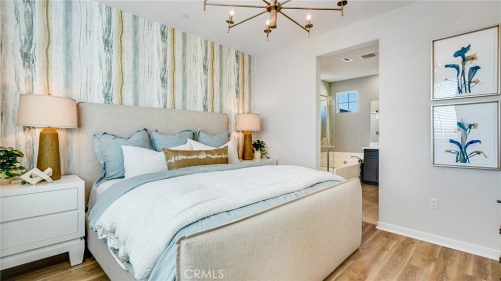 Bedroom on Montoya Paseo, Ontario, CA, with a beige upholstered bed, blue and white blankets, abstract wallpaper, and two bedside lamps.