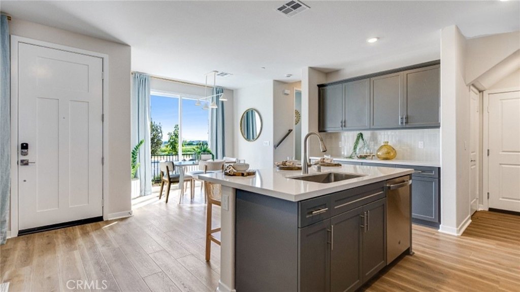 Kitchen and dining area on Exterior of a house on Montoya Paseo, Ontario, CA, with grey cabinets, white countertops, wood floors, and a large window.