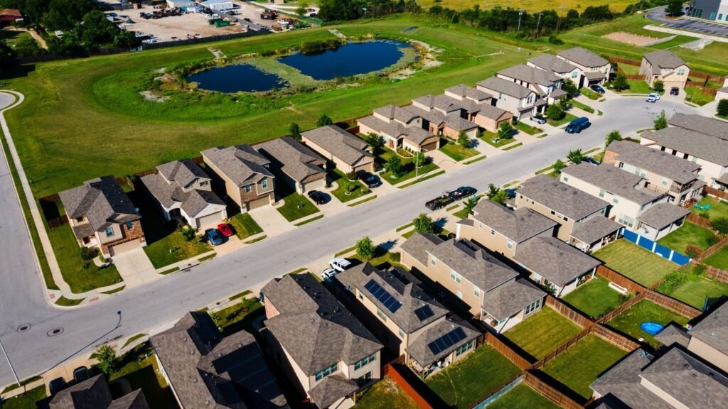 Aerial view of a California suburban neighborhood with brown-roofed houses, green lawns, and a small lake.