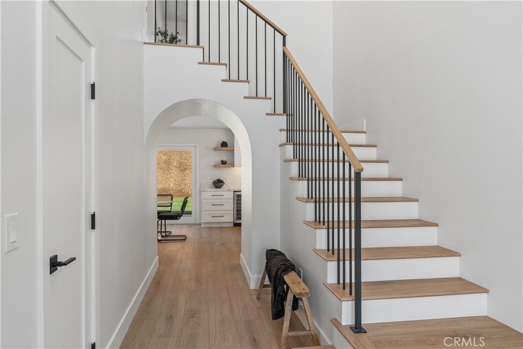 Modern California hallway on Cindy Ln in Lake Forest with wood floors, black staircase railings, and a bright dining room archway.